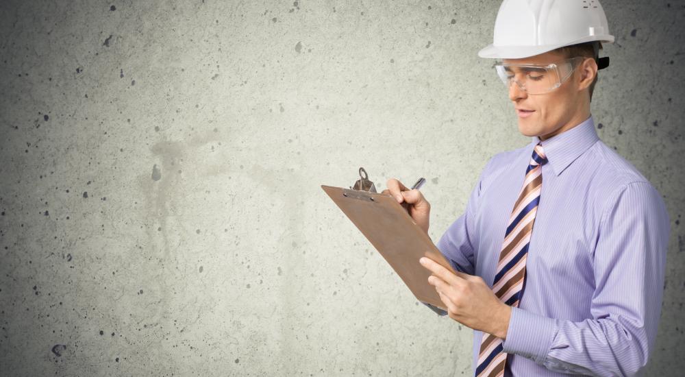 Image of a man in a white hardhat, purple collared shirt, striped tie, and safety glasses holding a clipboard and pen. 