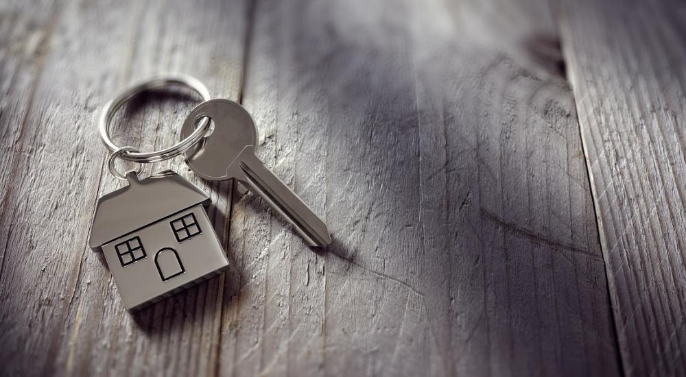 Image of a key on a wooden desk with a house shaped key ring attached. 